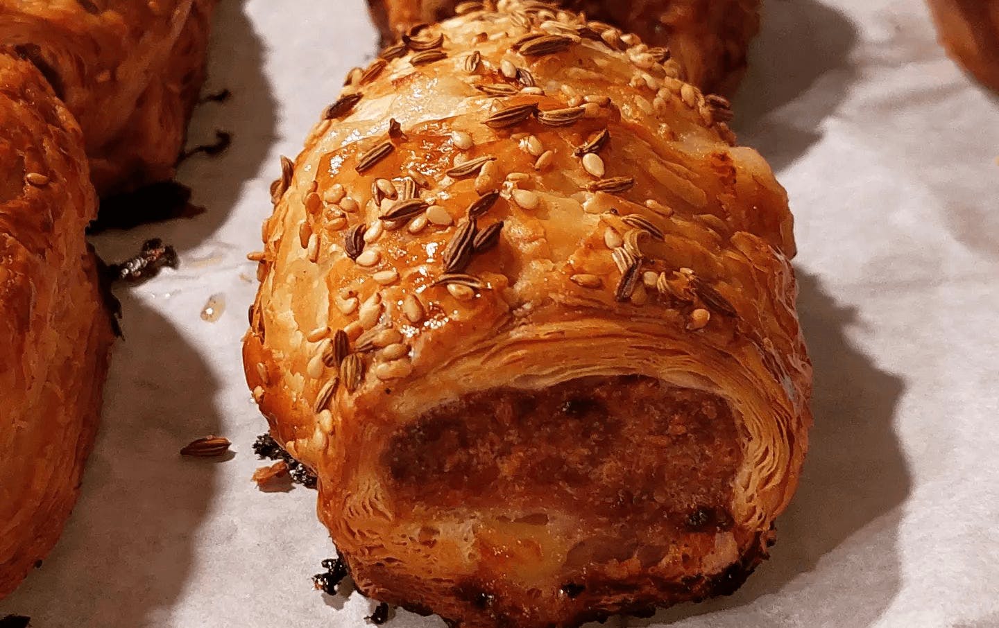 A thick sausage roll with sesame and fennel seeds on top. 