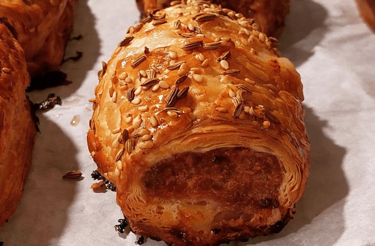 A thick sausage roll with sesame and fennel seeds on top. 