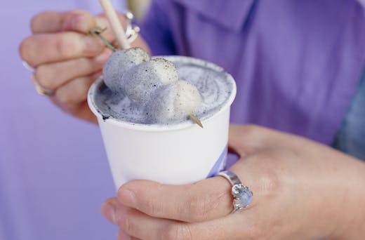 A black sesame latte topped with three mochi balls on a skewer.