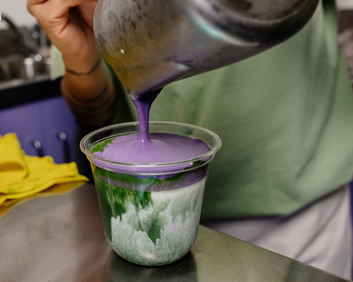 Ube is poured on top of matcha in a takeaway cup. 