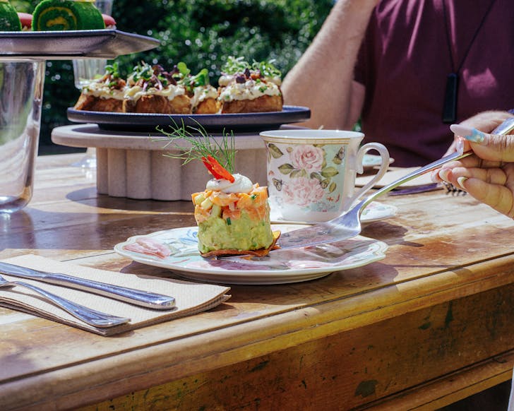 Someone with mermaidcore nails selects a treat from the high tea at Farm House Cafe. 