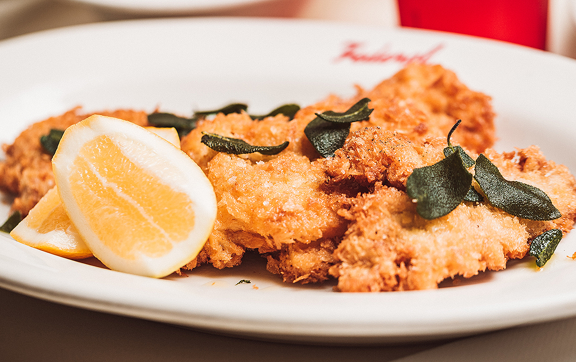 A delicious looking schnitzel from Federal Delicatessen sitting on a plate with crispy sage leaves on top and a slice of lemon.