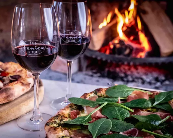 Two glasses of red wine and meals on a table in front of a fireplace at Cafe Fenice. 