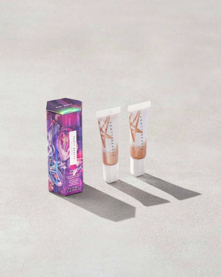 A purple and pink hexagonal shaped box standing beside two white and bronze tubes of liquid highlighter.