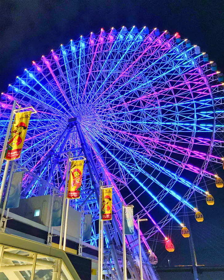 The vibrant, brightly lit giant ferris wheel towers over Osaka Bay at nighttime. 