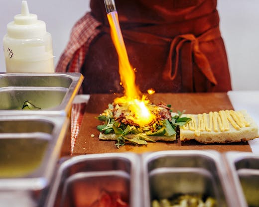 A chef torches some the cheese on a sandwich with a blow torch. 