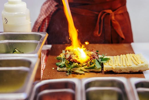 A chef torches some the cheese on a sandwich with a blow torch.