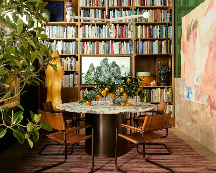 An interior shot of a Flack Studio library space featuring a large, built in bookshelf and a sleek and modern designed room. There is colourful art along the wall and indoor plants complimenting the space.