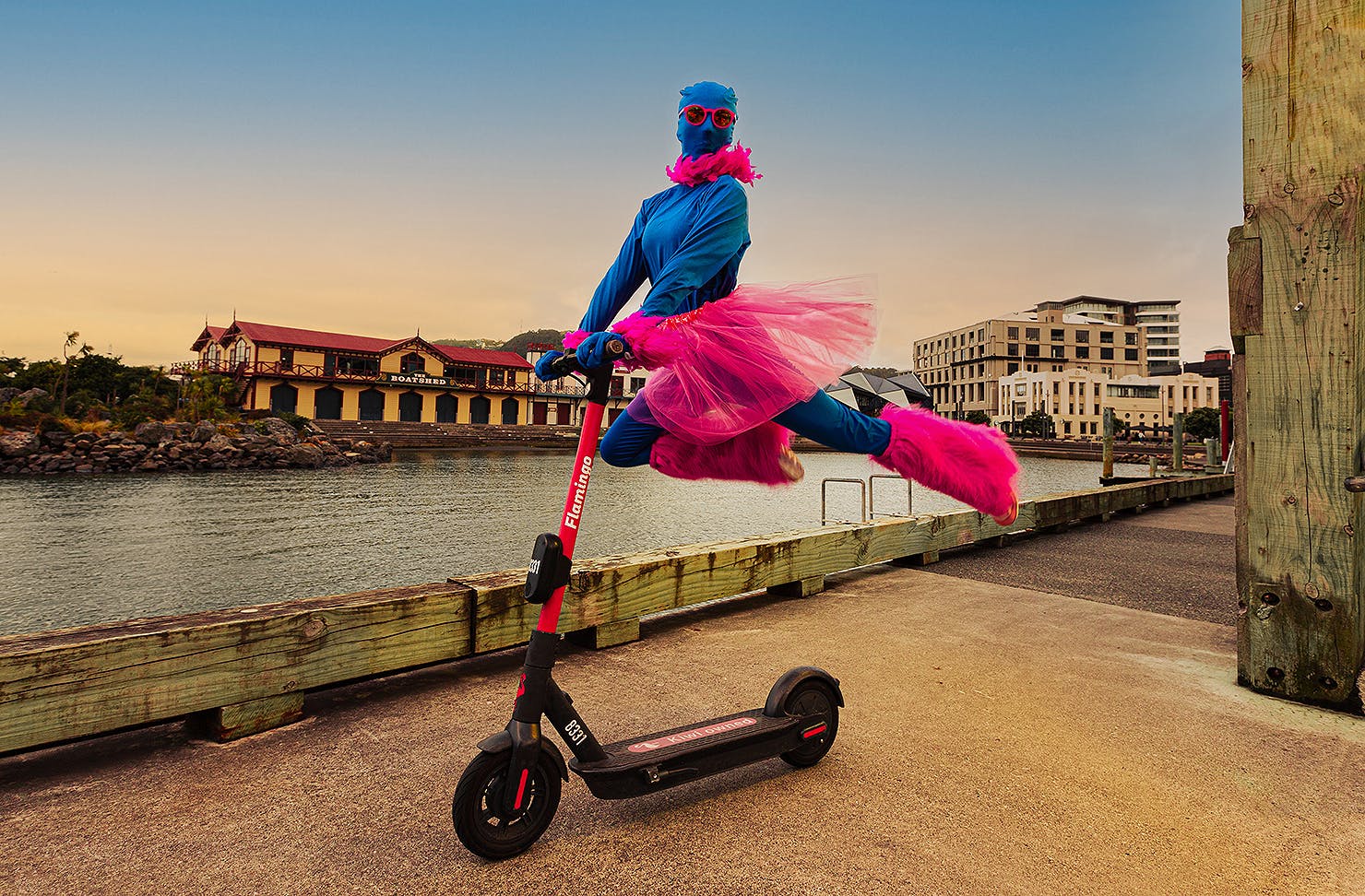 A person dressed in pink and blue leaps on the back of a scooter, cutting a dramatic figure.