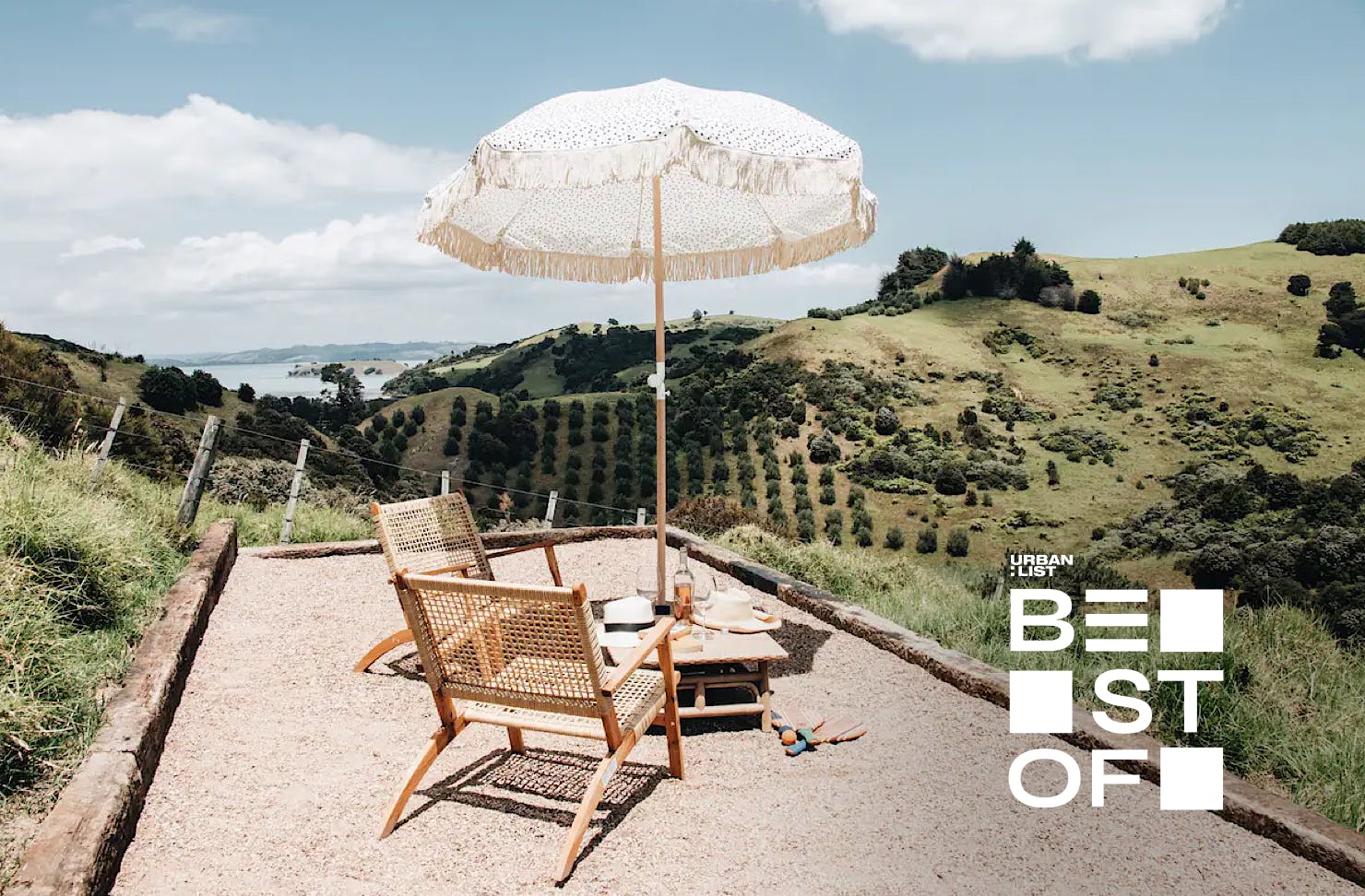 A darling chair and umbrella set up overlooking rolling hills and the ocean at Fleetwood, one of the best Airbnbs on Waiheke Island. 