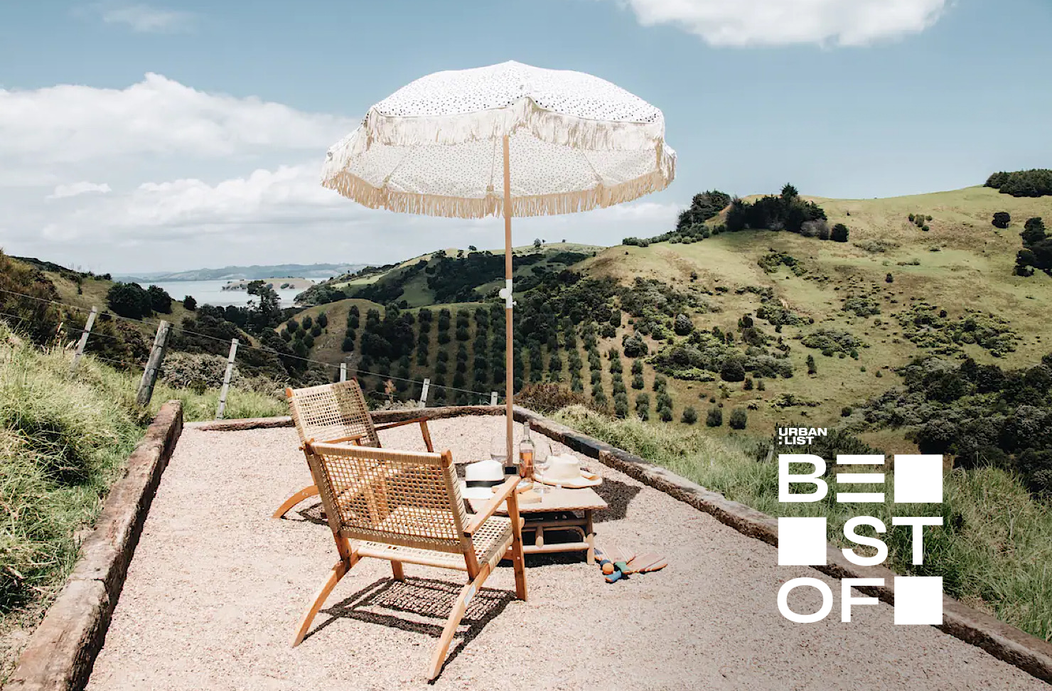 A darling chair and umbrella set up overlooking rolling hills and the ocean at Fleetwood, one of the best Airbnbs on Waiheke Island. 