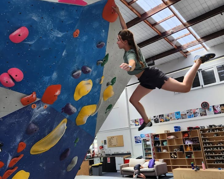 A woman hangs by one hand off a bouldering wall. 