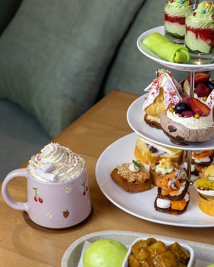 A three-tier high tea stack of goodies and a mug of tea with whipped cream and little marshmallows. 