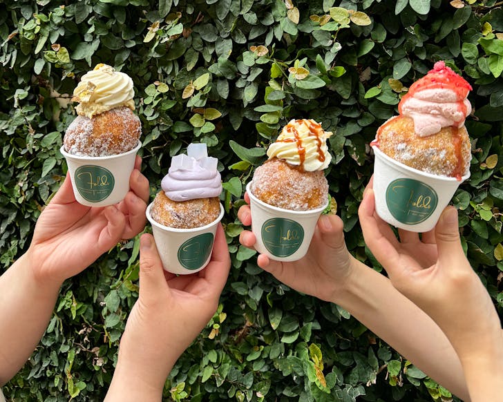 Four hands holding up deep fried balls of gelato. 