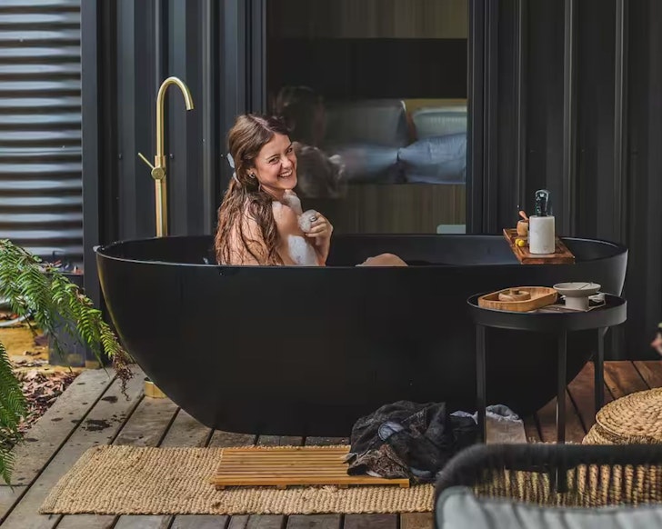 A woman soaking in a black outdoor bath at Forrest Haus Retreat Victoria
