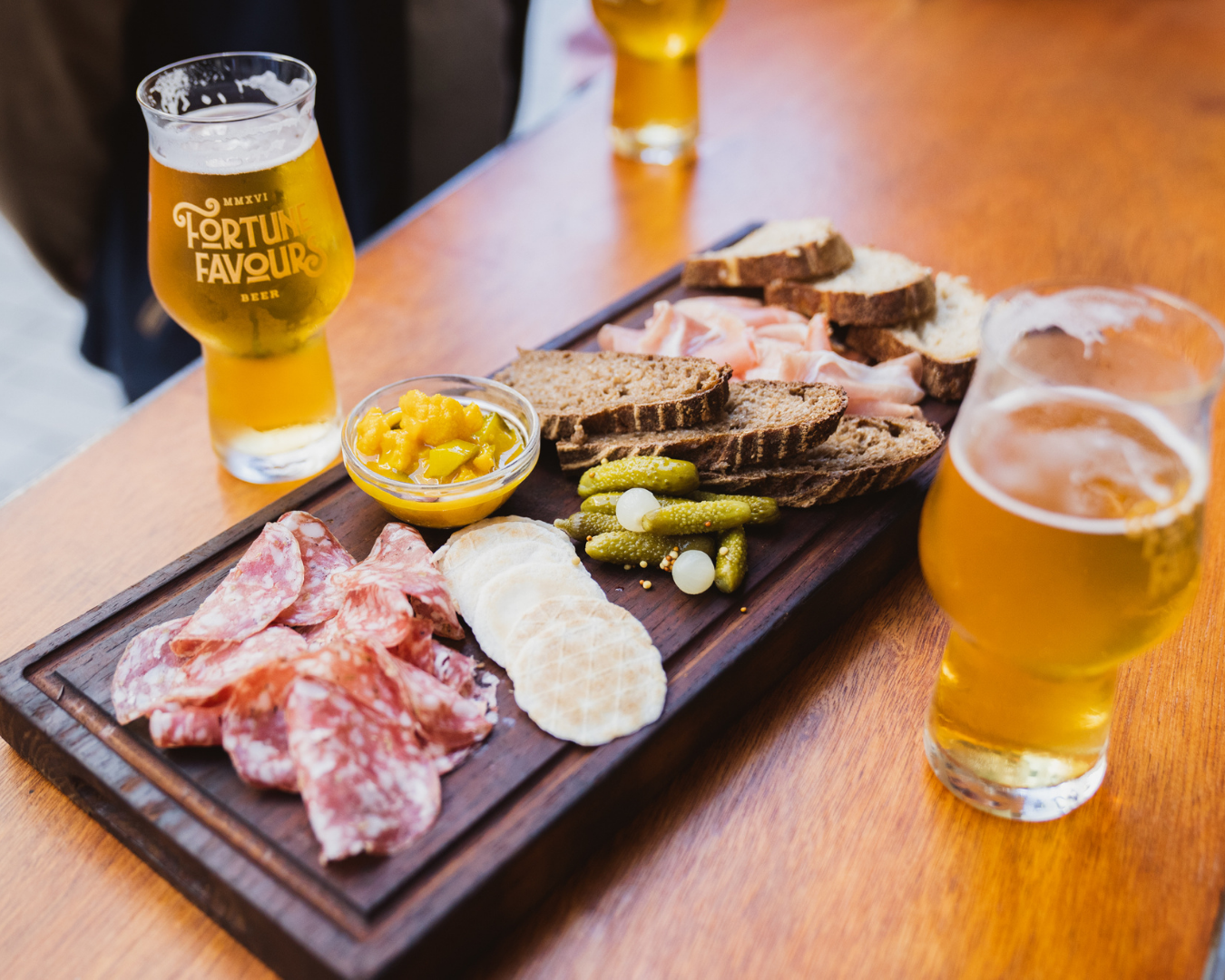 A beautiful graze board with cold cuts, bread and condiments alongside pints of fortune favour beers