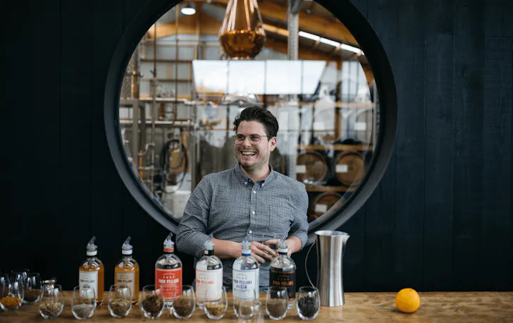 A person smiling with a selection of gin bottles in front of him. 