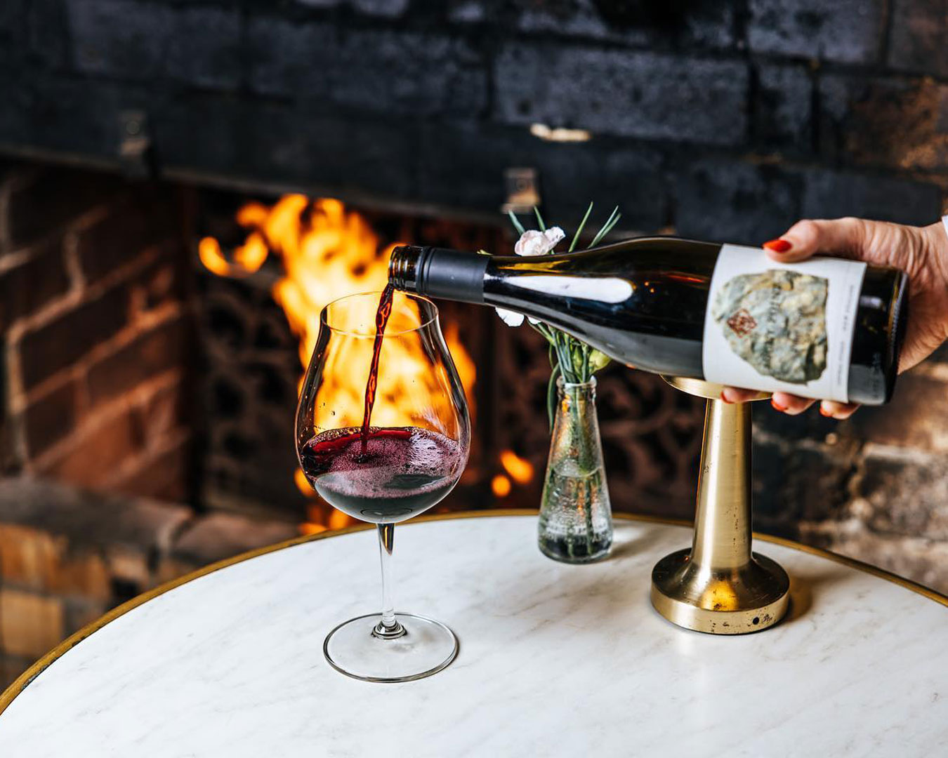 Red wine pouring into a glass in front of fireplace