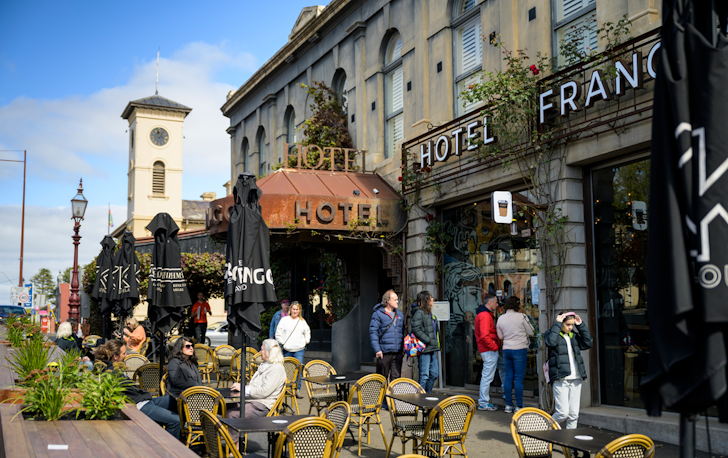 A busy street with people walking past and dining in front of Hotel Frangos