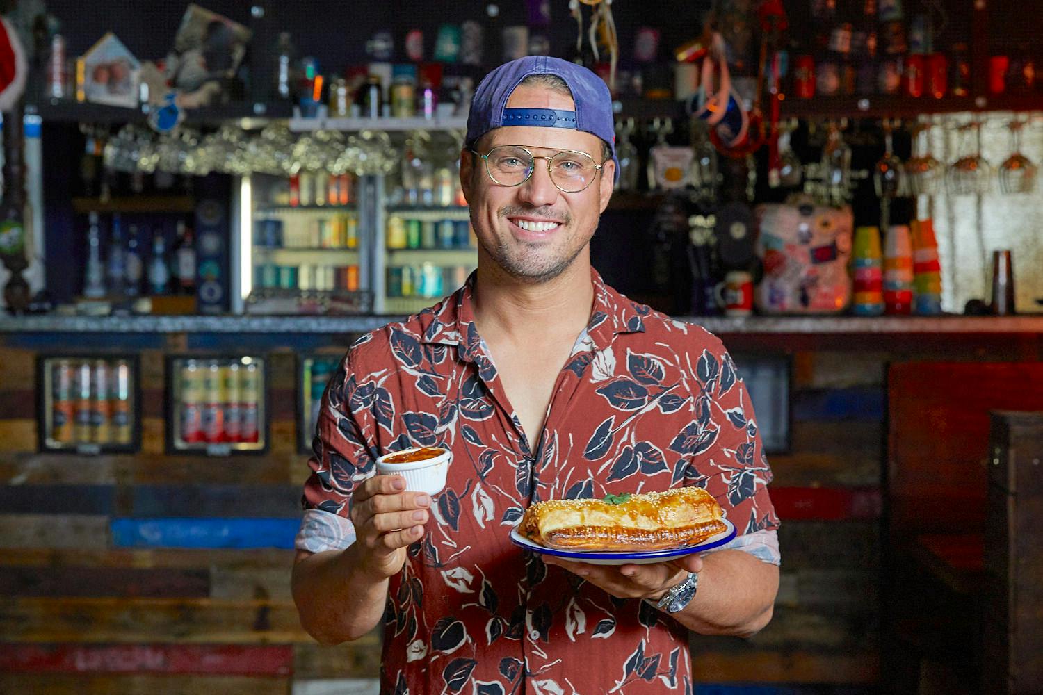 Wings x Tins Anthony MacFarlane holds up his spicy sausage roll. 