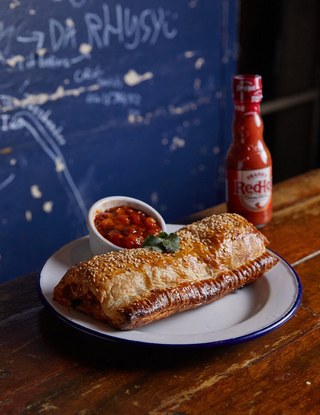 A glorious golden sausage roll sitting next to Frank's RedHot Sauce.