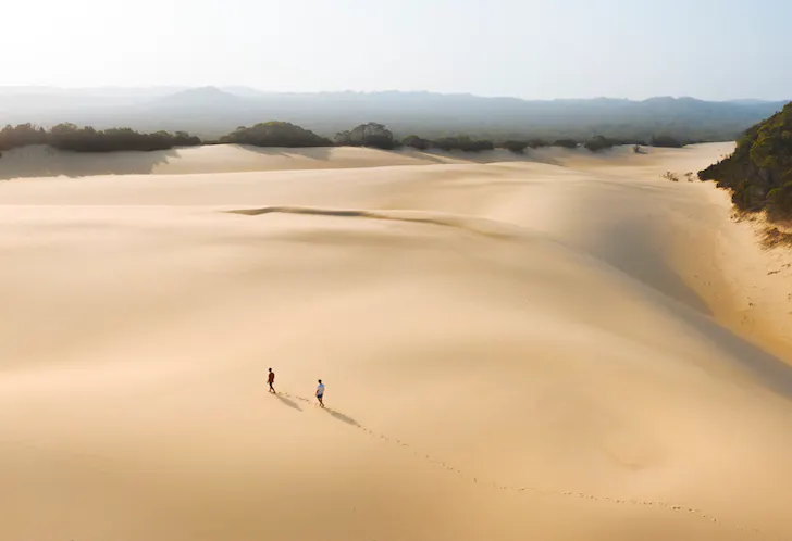 Two people trek across a vast and untouched sand blow on Fraser.