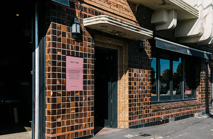 The exterior entrance to Free To Feed with brown tiling and a pink sign.