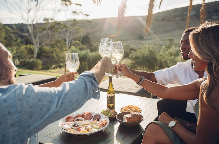 Friends clinking glasses of wine while sitting outside at Stonyridge vineyard on Waiheke