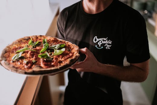 A man with a black t-shirt holding a pizza.