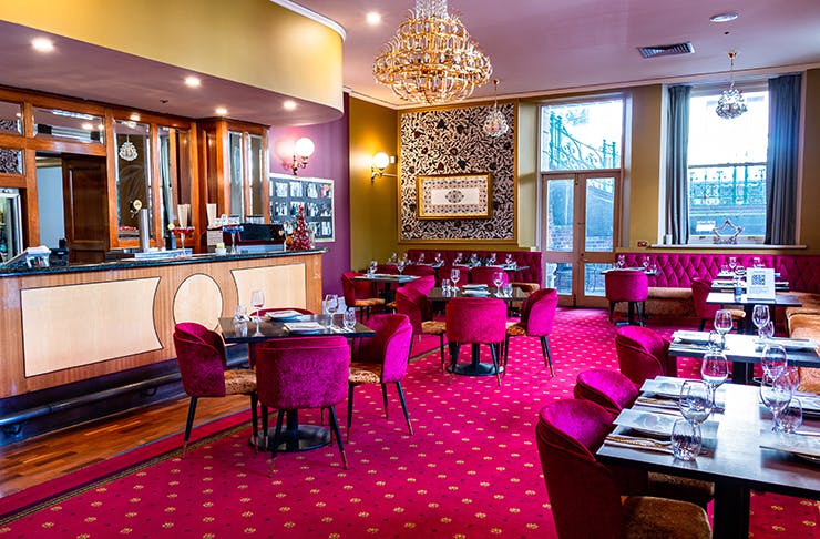 a dining area with pink suede chairs, a wooden bar, and pink carpet with gold coloured patterns throughout