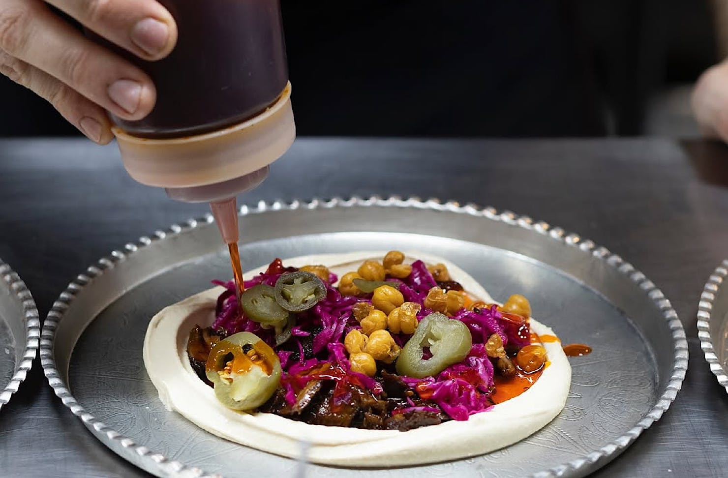 Someone squeeze some sauce onto a stacked tray of hummus.