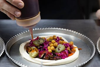 Someone squeeze some sauce onto a stacked tray of hummus.