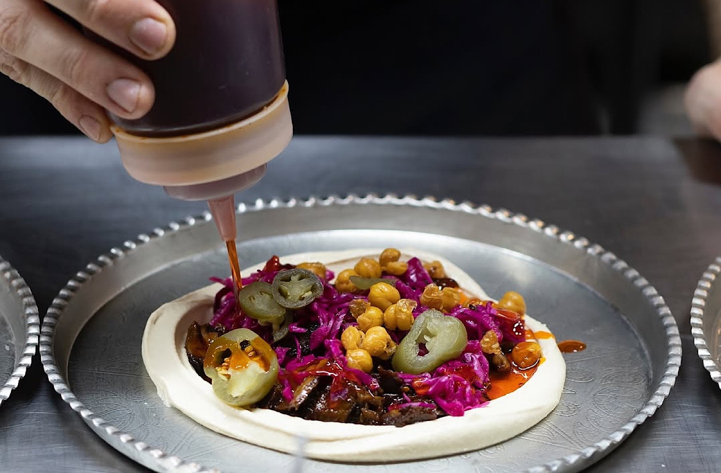 Someone squeeze some sauce onto a stacked tray of hummus.