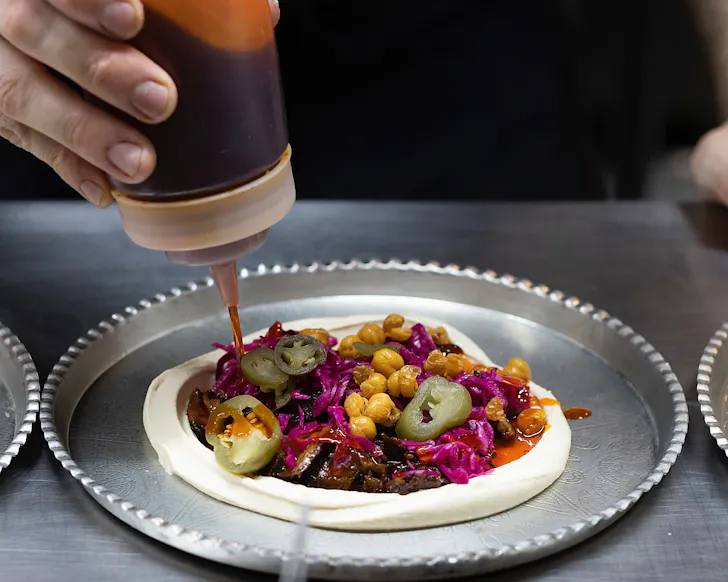Someone squirts sauce onto Gemmayze St's iconic hummus.