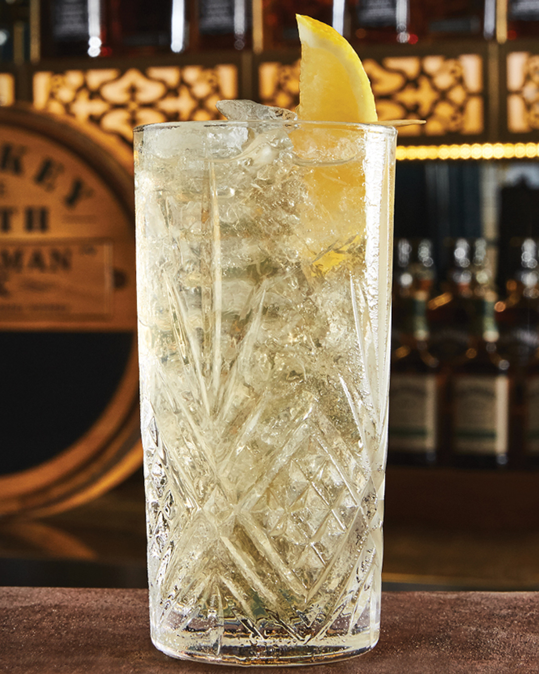 A Gentleman's Highball garnished with a lemon wedge on a bar.