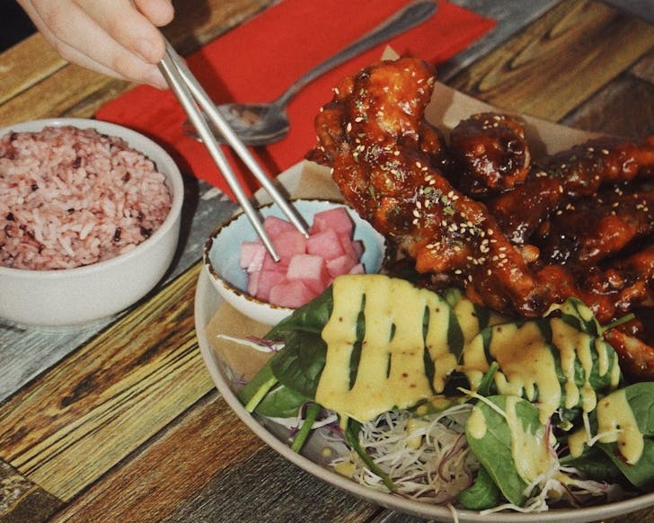 Chopsticks digging into a dish of spicy marinated pork ribs, rice and side dishes.