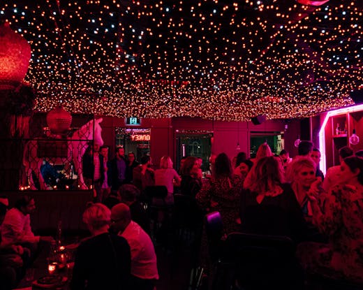 An inside of a bar with neon-lights with people drinking. 