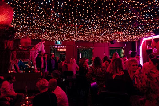 An inside of a bar with neon-lights with people drinking.