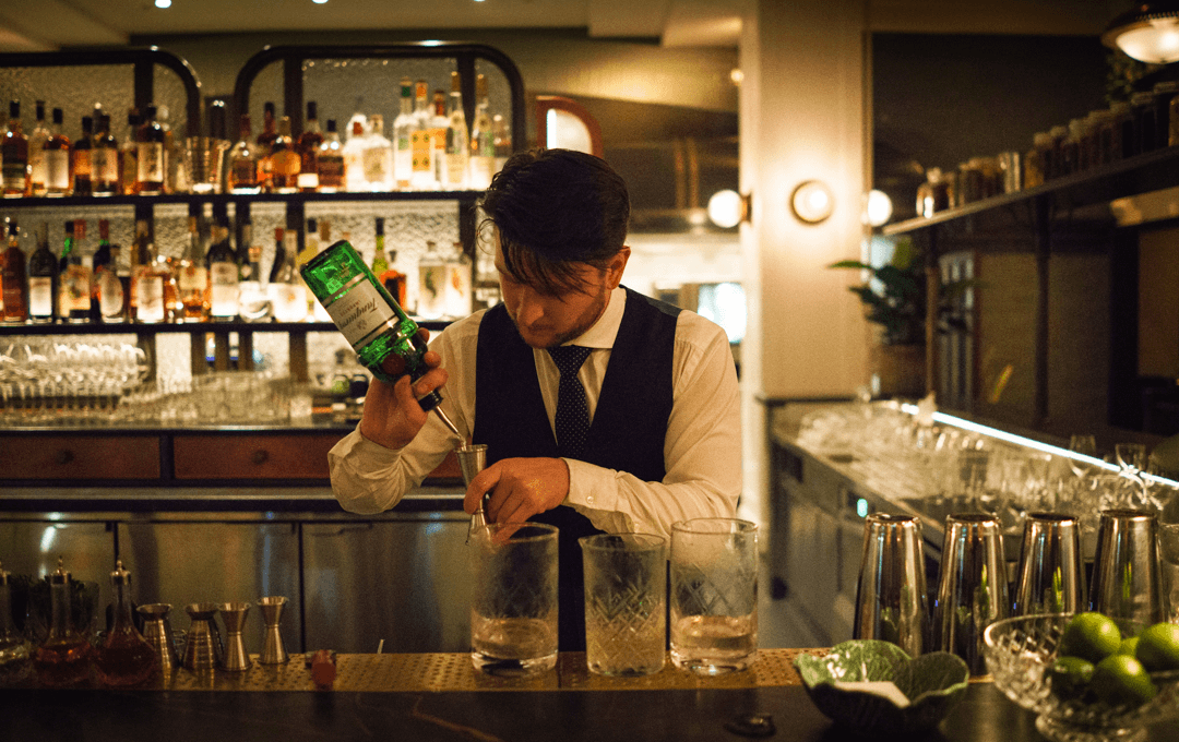 A bartender in a white shirt pouring a bottle at a cocktail bar Melbourne cbd. 