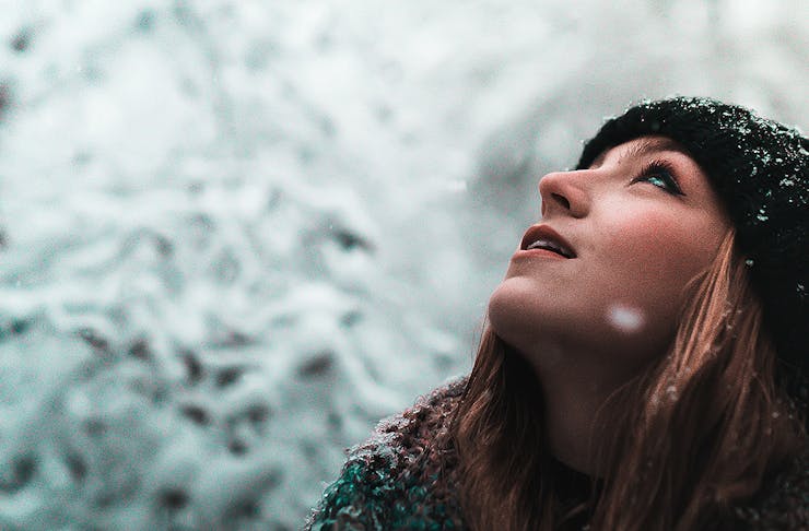 A girl looks up in the snow, wrapped up against the elements.