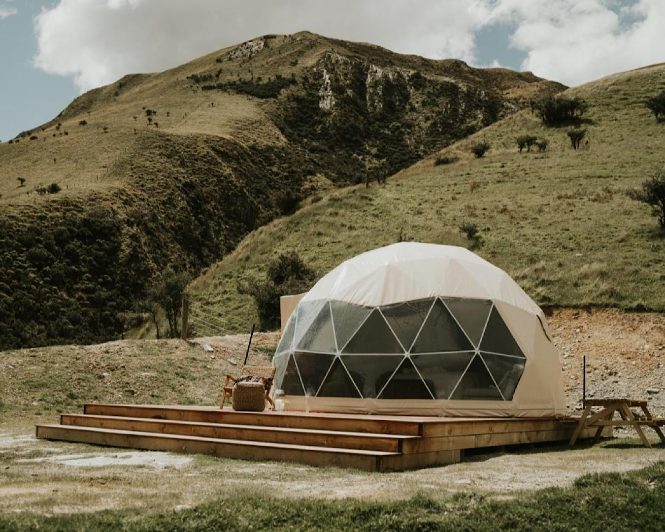 A geodesic dome sits in a field on a backdrop of rolling hills.