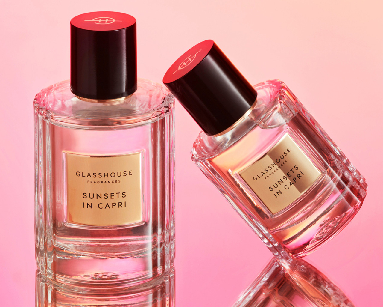 Two glass bottles of perfume with gold labels with 'Sunsets in Capri' against a pink backdrop.