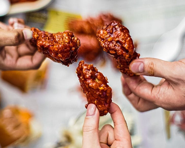 Three people hold up fried chicken from Gochu, one of the best fried chicken joints in Auckland.