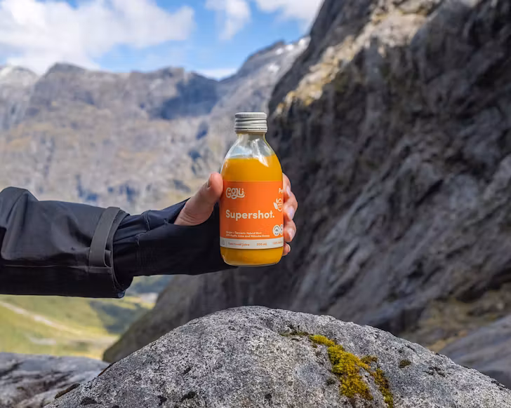 Someone holds a small bottle of Goju supershot over a mossy rock in the great outdoors. 