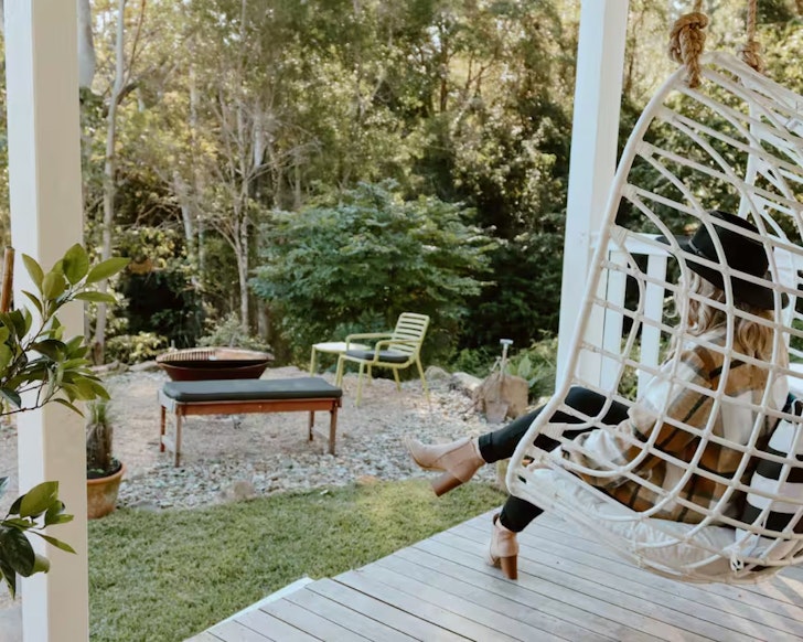 A woman swings on the egg chair overlooking the garden at Gracie Cottage Airbnb one of the best accommodation options near Maleny
