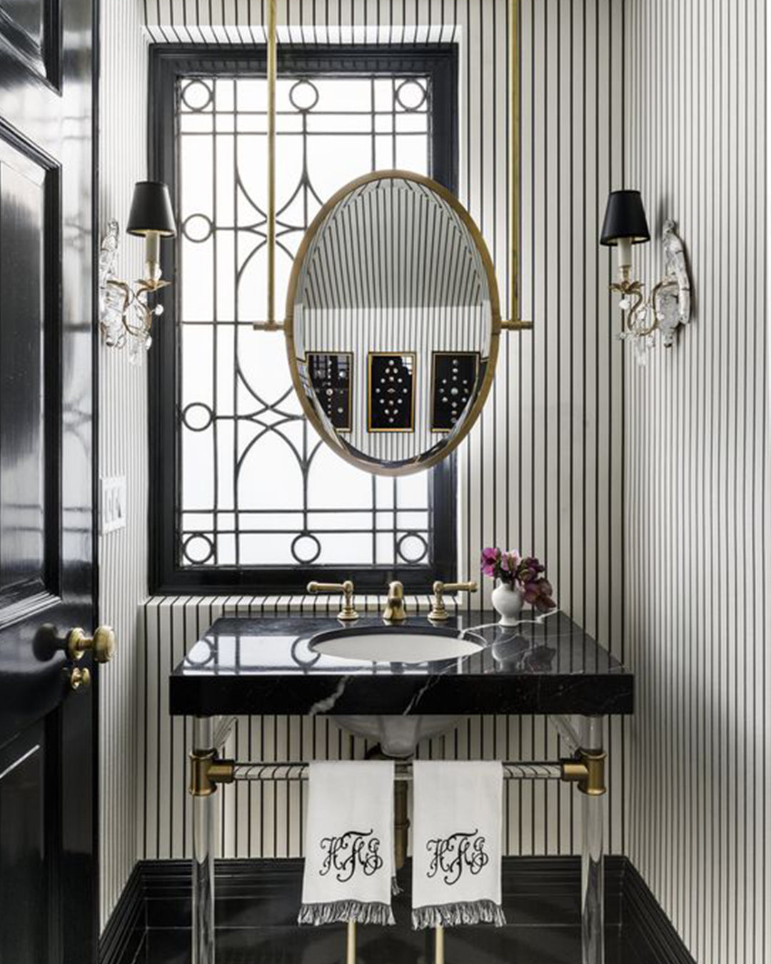 Grand Millenial style bathroom with gold oval mirror, striped wallpaper and black accents