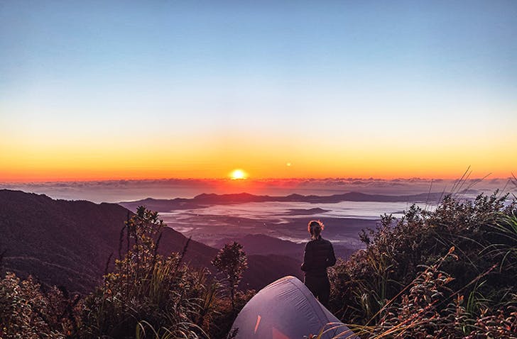 A woman on top of a hill with a tent looking at a sunset.