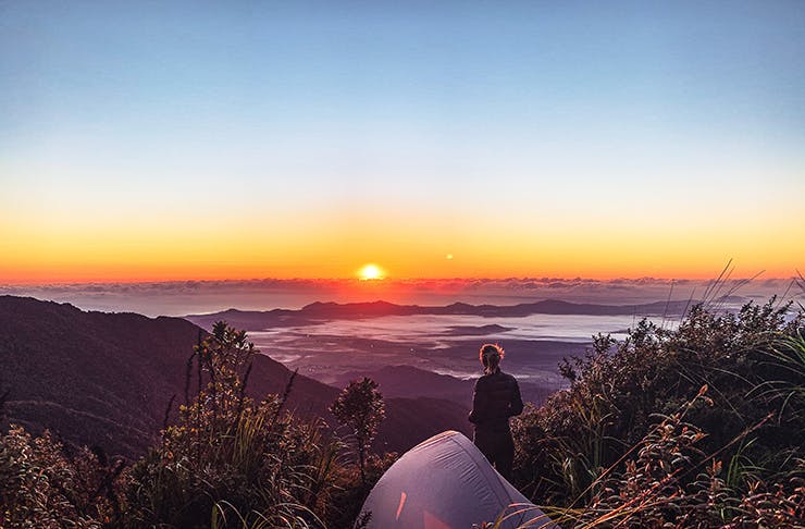 A woman on top of a hill with a tent looking at a sunset.