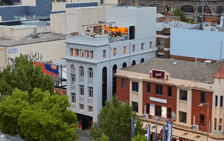 A large white building with a busy rooftop bar with people on it.