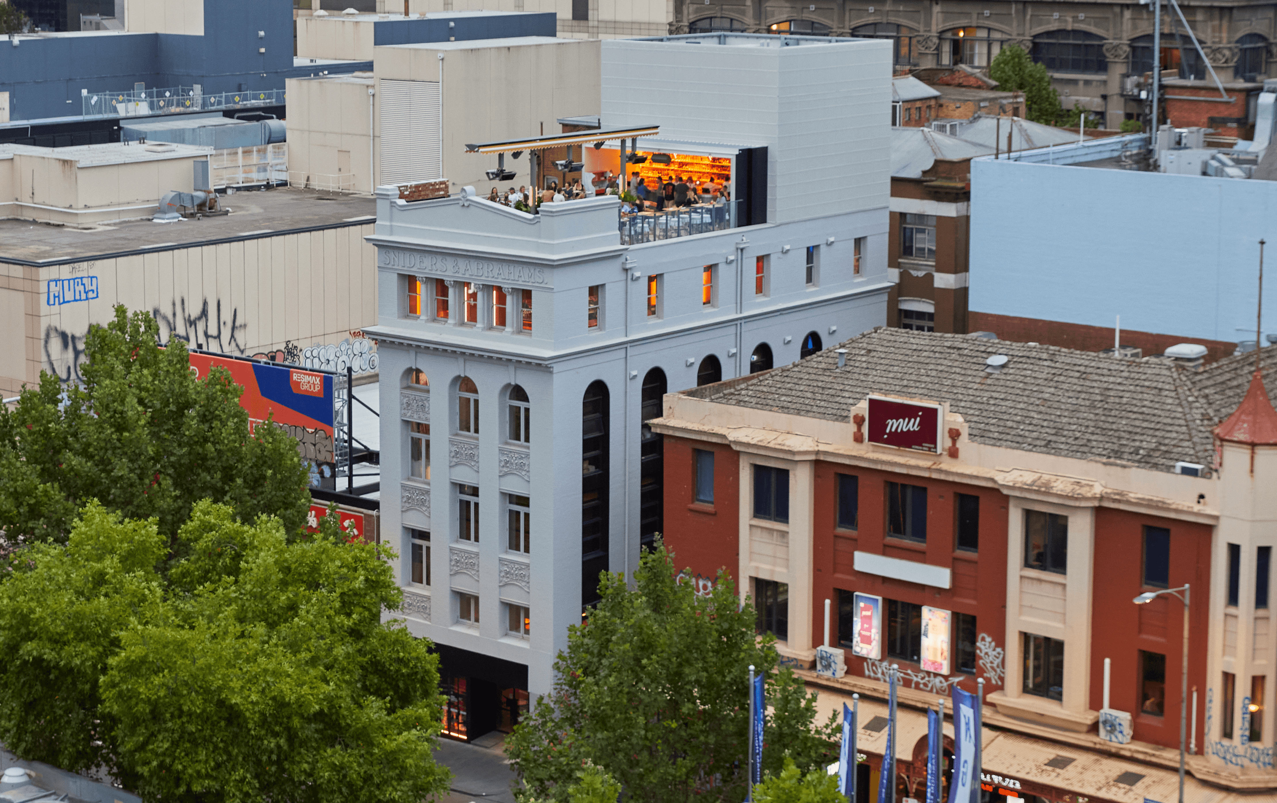 A large white building with a busy rooftop bar with people on it.